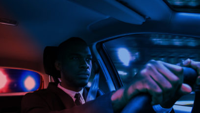 Black man behind wheel of automobile, red and blue lights