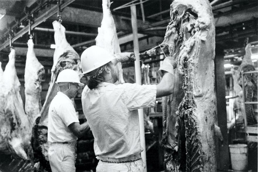 In this photo from 1990, two meatpacking workers trim beef carcasses inside the plant near Garden City.