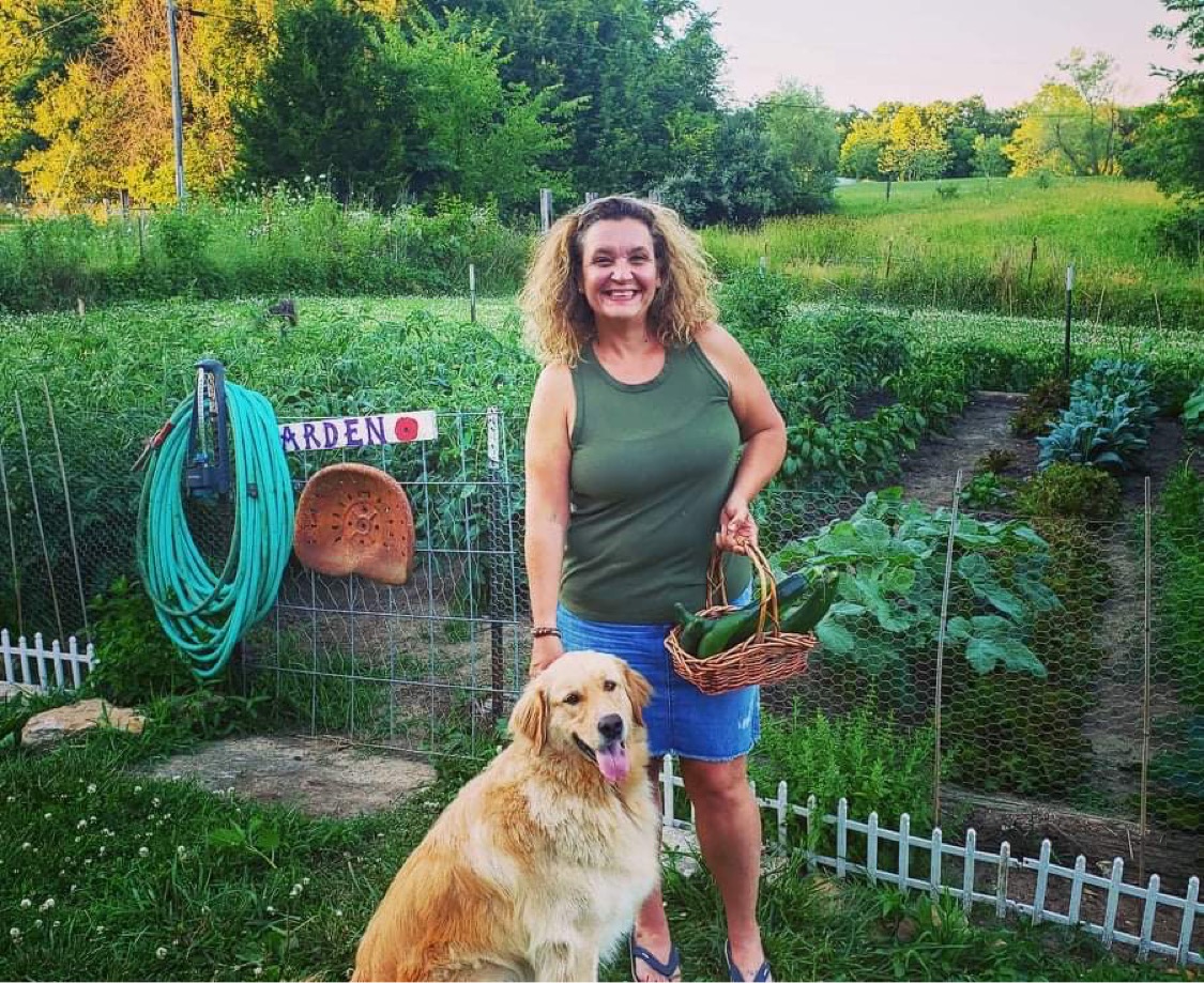 Woman smiles with golden retriever in front of vegetable garden