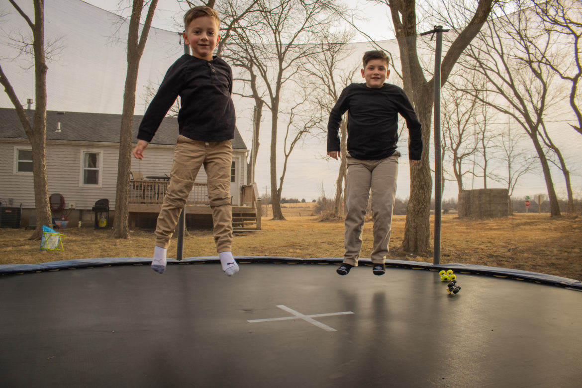 Two young boys jump on trampoline.
