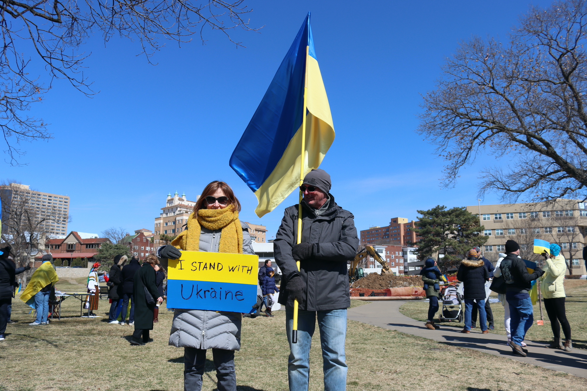 Woman holds sign that reads "I stand with Ukraine" man next to her holds Ukrainian flag.