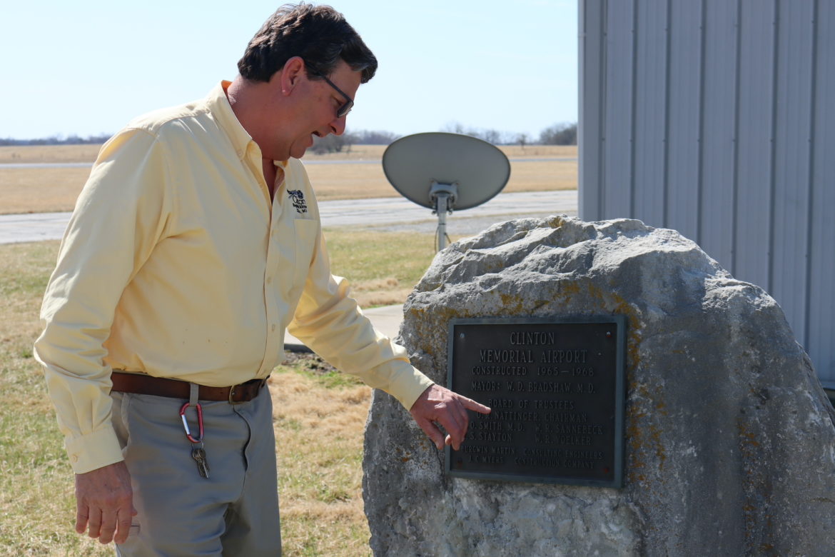 Man in yellow shirt points to a rock monument dedicated to the founders of the airport.