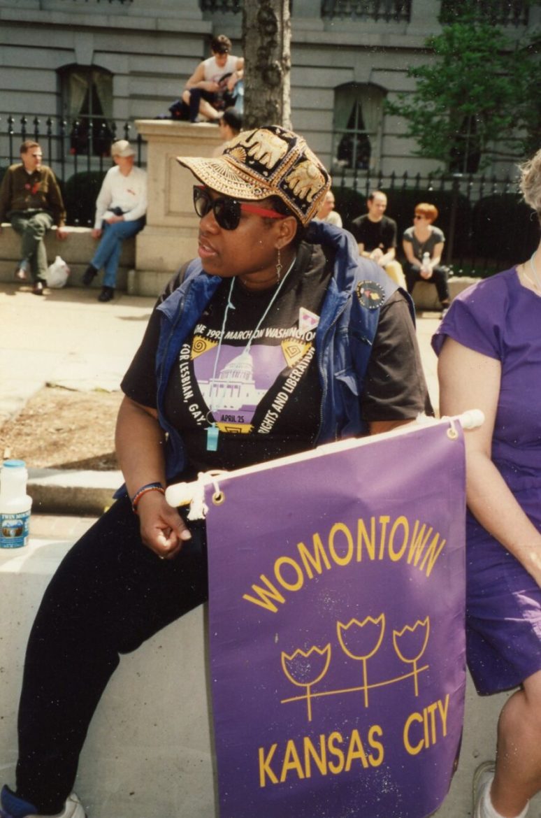 Womontown residents identified one another by hanging purple and yellow tulip flags on their doors. Here, Beverly Powell carries a Womontown flag. In the Womontown documentary, Powell’s partner Sue Moreno celebrates her for being the first African American woman to buy a house in Womontown.