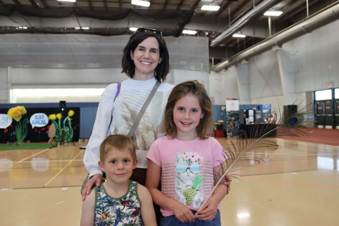 Mom with daughter and son in a gymnasium. Daughter holds peacock feather.
