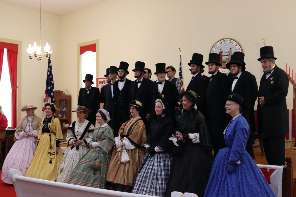 Men dressed as Abraham Lincoln pose in the back row with women dressed as Mary Todd Lincoln in the front row.