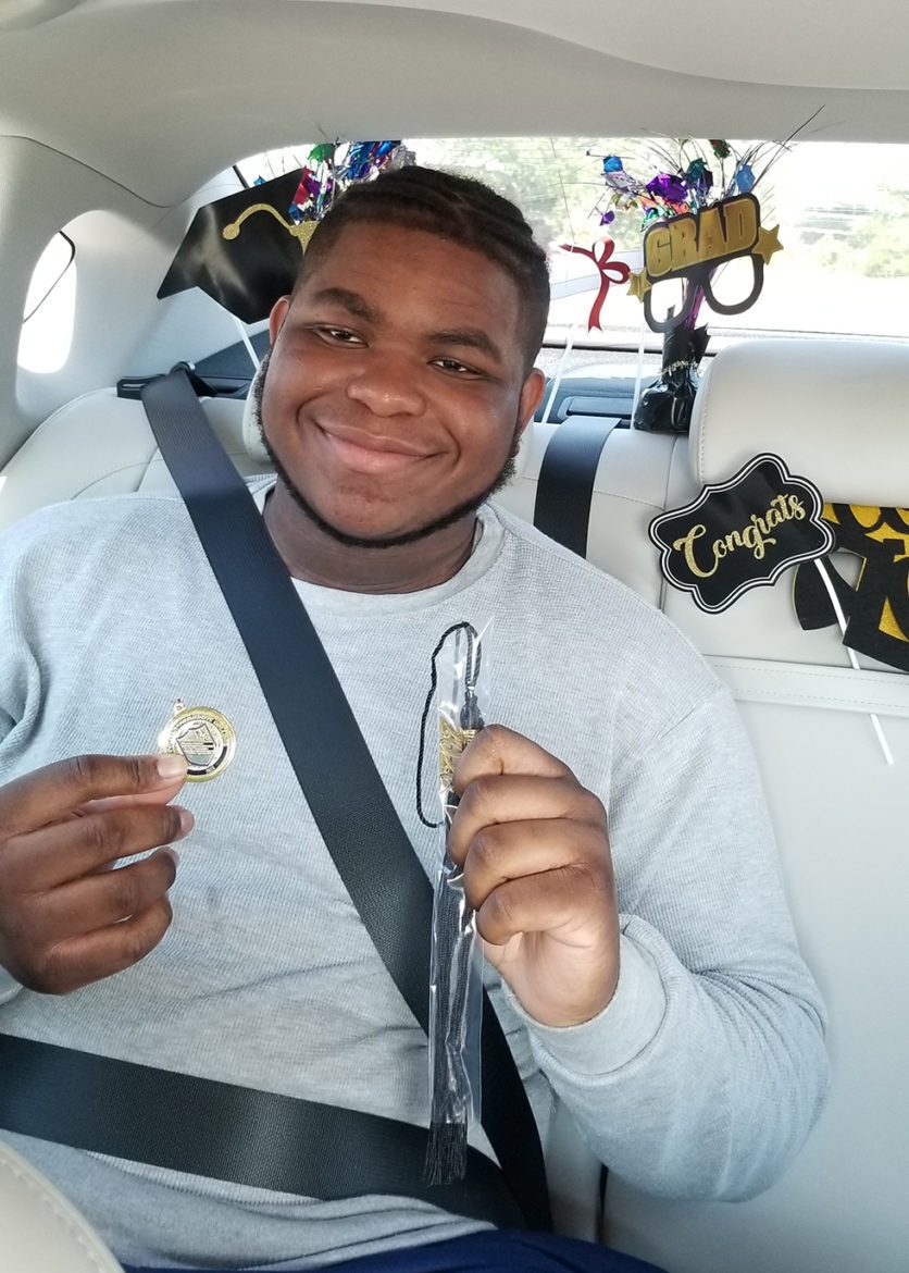 Juleon Dillard, 19, smiles at his drive-through graduation, holding his tassel in one hand and a pin in the other