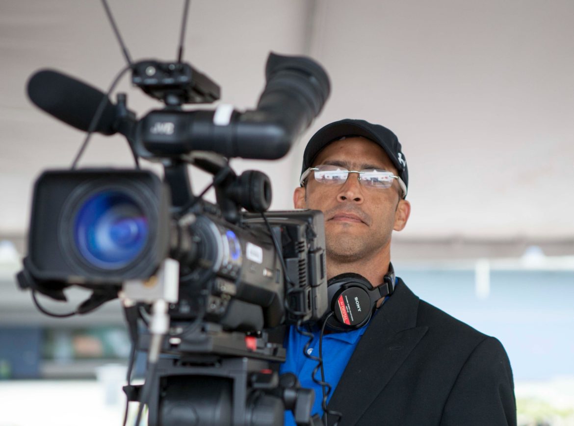 Yosmel Serrano stands behind a camera.