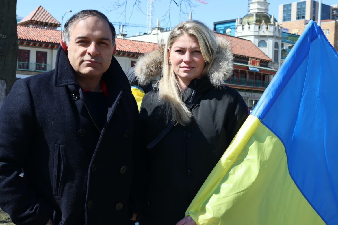 Man left, woman right holding Ukrainian flag. Country Club Plaza visible behind the couple.